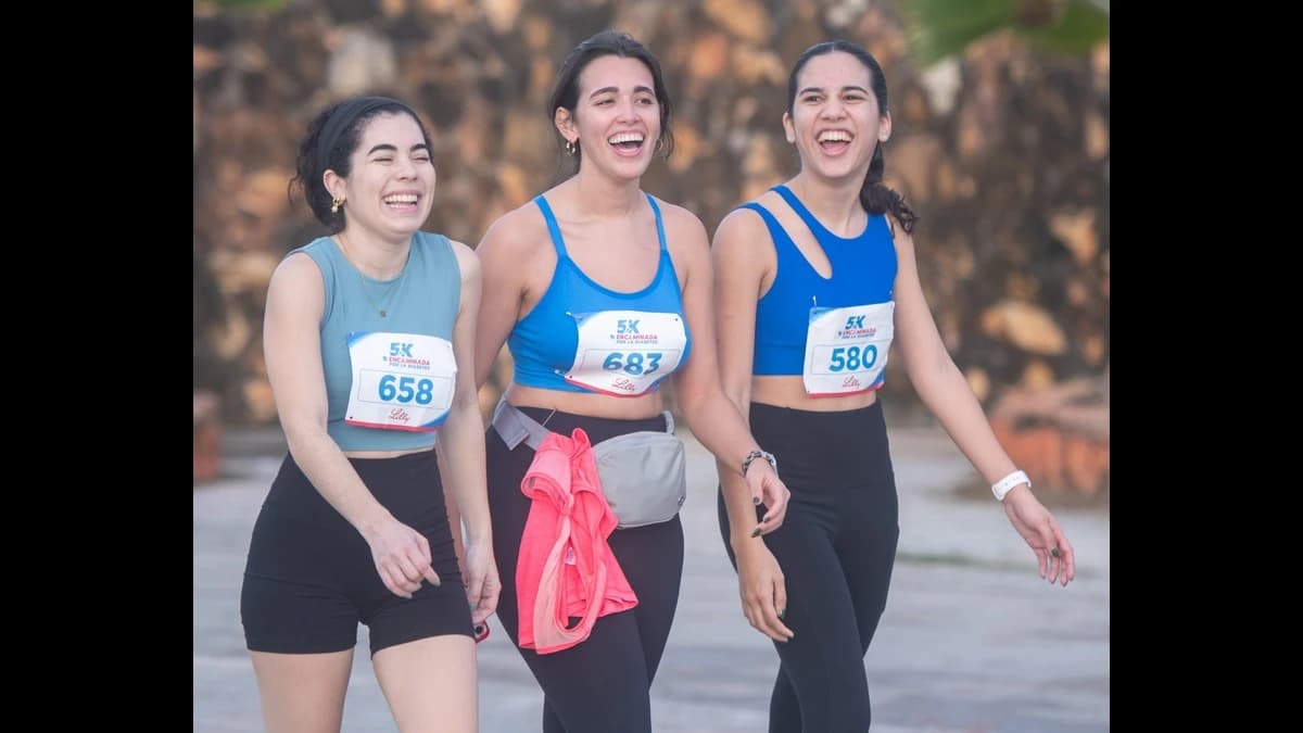 Tres mujeres jóvenes con números de corredor sonríen mientras caminan juntas durante la Encaminada 5K por la Diabetes en el Escambrón, San Juan.