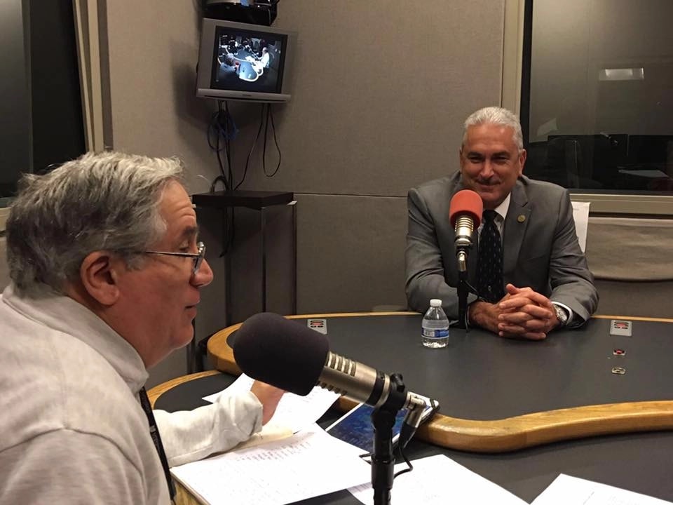 Luis Dávila Colón conversa frente a un micrófono en un estudio radial mientras Thomas Rivera Schatz lo escucha al otro lado de la mesa. (Imagen suministrada)