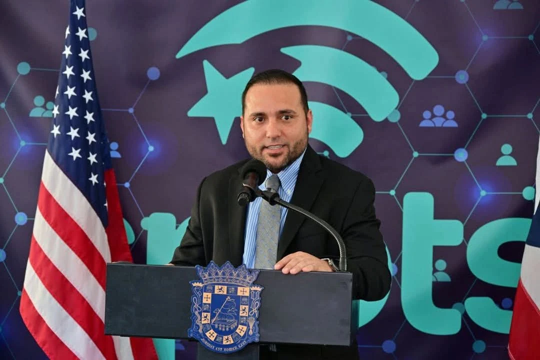 Orlando Rivera Berríos, director de la OGP, ofrece declaraciones en una conferencia de prensa del programa Smart Island, con banderas de Estados Unidos y Puerto Rico al fondo. Imagen tomada de redes sociales.