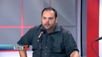 Hombre de cabello oscuro y barba corta, con camisa negra de botones, sentado frente a un micrófono en un estudio de televisión con paneles rojos y grises al fondo. En la esquina inferior izquierda aparece el logo del programa Nación Z.