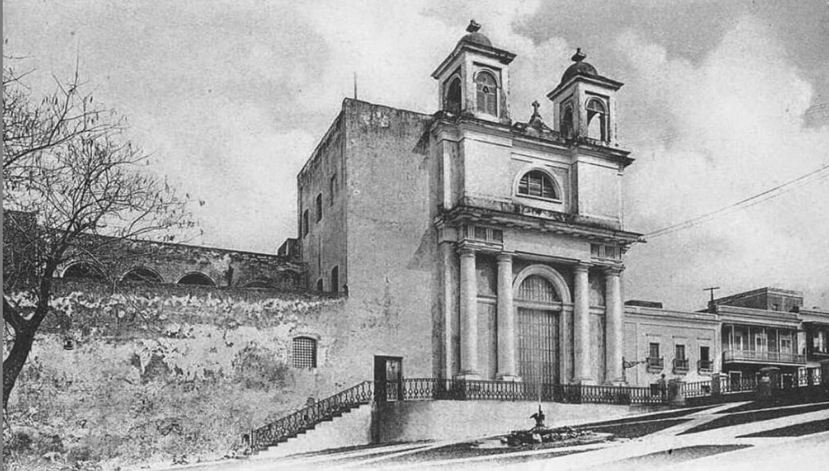 Fotografía histórica en blanco y negro del edificio del antiguo convento de las Carmelitas en el Viejo San Juan, con sus dos torres campanario, fachada con columnas y arcos, y los muros de piedra del convento original visibles a la izquierda.