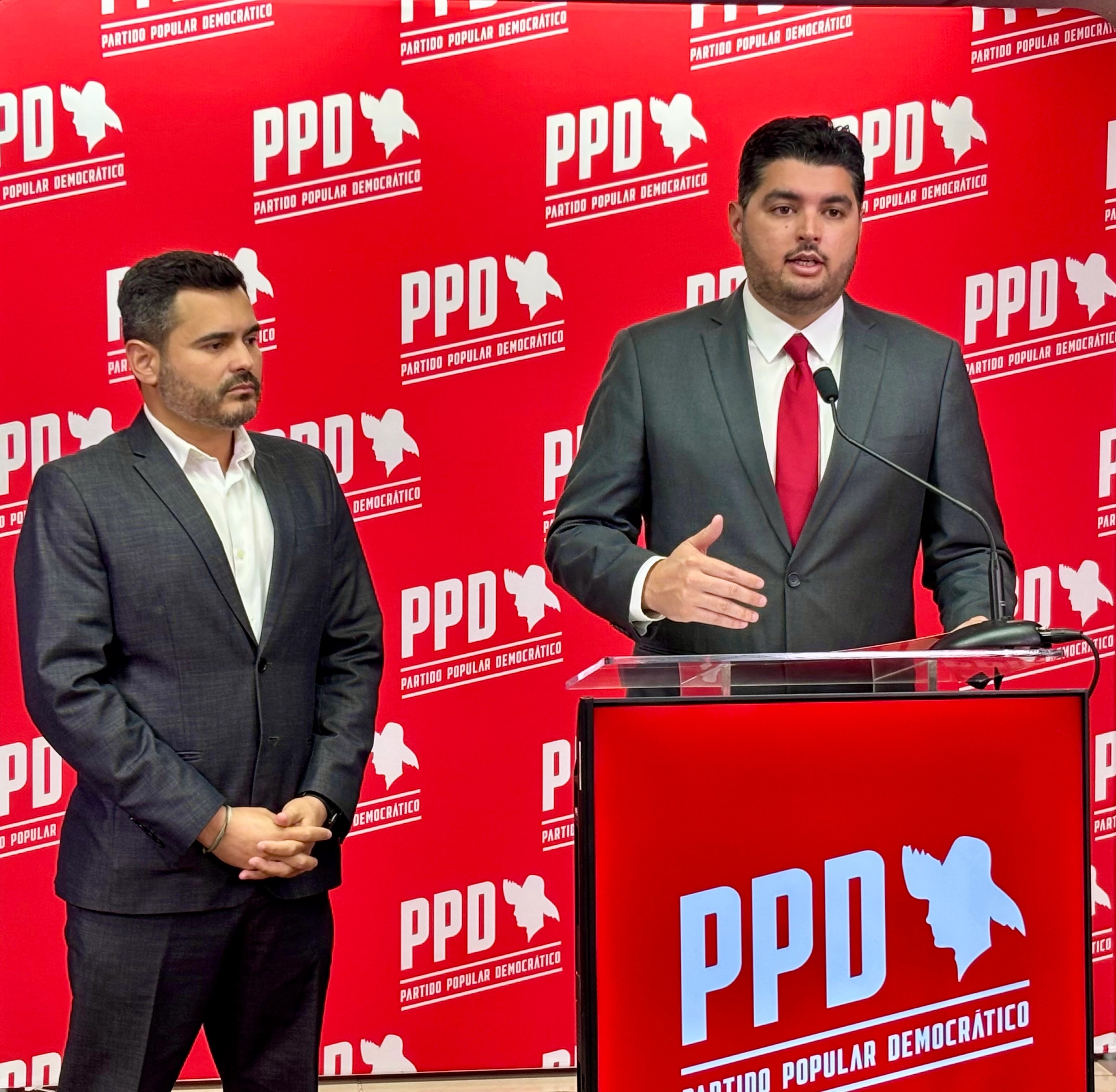 Manuel Calderón Cerame ofrece declaraciones en un podio del PPD mientras Olvin Valentín permanece a su lado, frente a un fondo con el logo del Partido Popular Democrático. (Imagen suministrada)