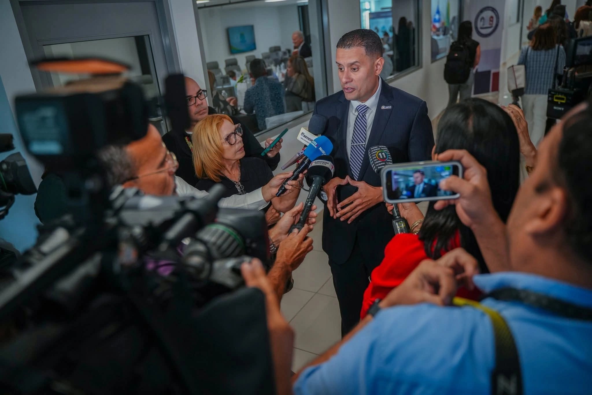 Gabriel Hernández, presidente de la Federación de Alcaldes de Puerto Rico, habla ante micrófonos de varios medios de comunicación rodeado de periodistas y camarógrafos en un pasillo institucional.