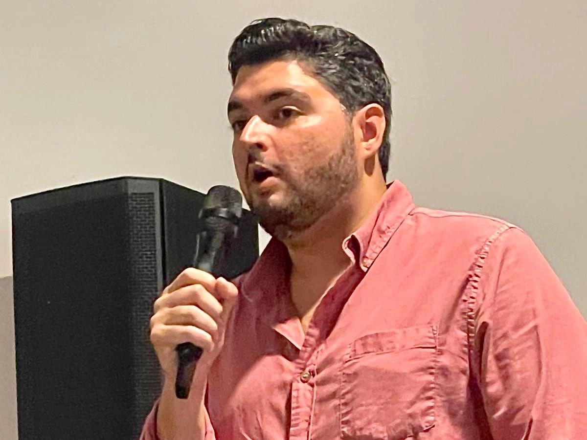 Manuel Calderón Cerame sostiene un micrófono mientras ofrece expresiones en una actividad política, vestido con camisa roja y frente a un equipo de sonido.