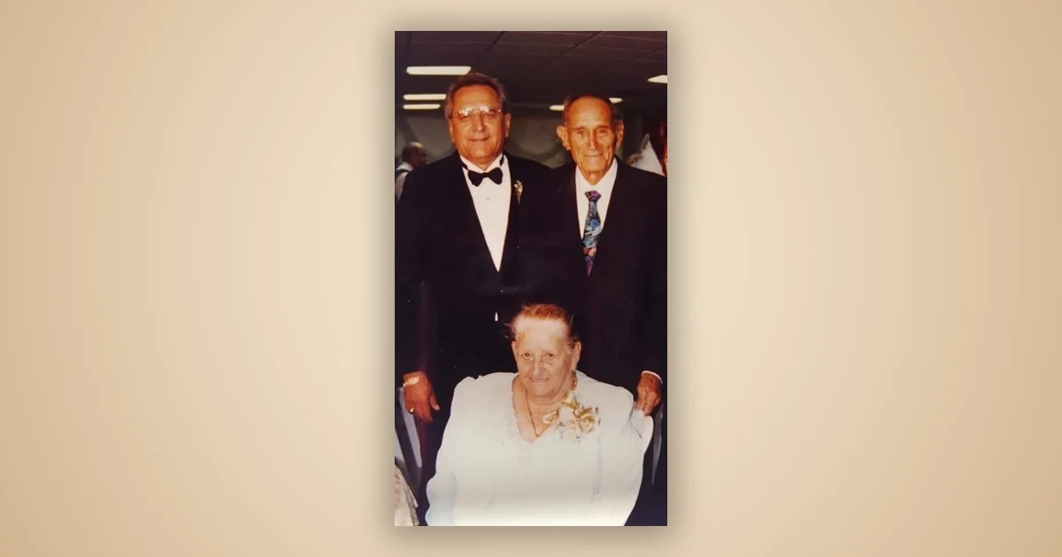 Rosario Díaz Pacheco, abuela del autor, sentada al frente vestida de blanco con un corsage de flores; detrás de ella, dos familiares en traje formal posan de pie.