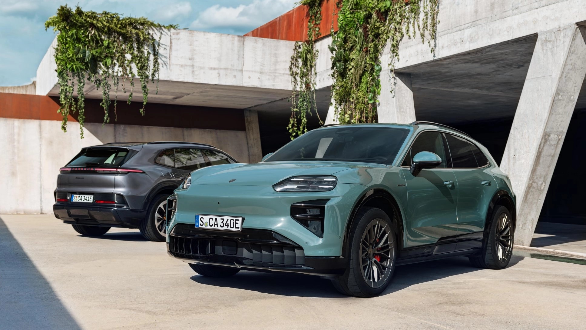 Dos vehículos Porsche Cayenne Electric estacionados frente a una estructura arquitectónica moderna, destacando el diseño exterior del SUV eléctrico en un entorno urbano.