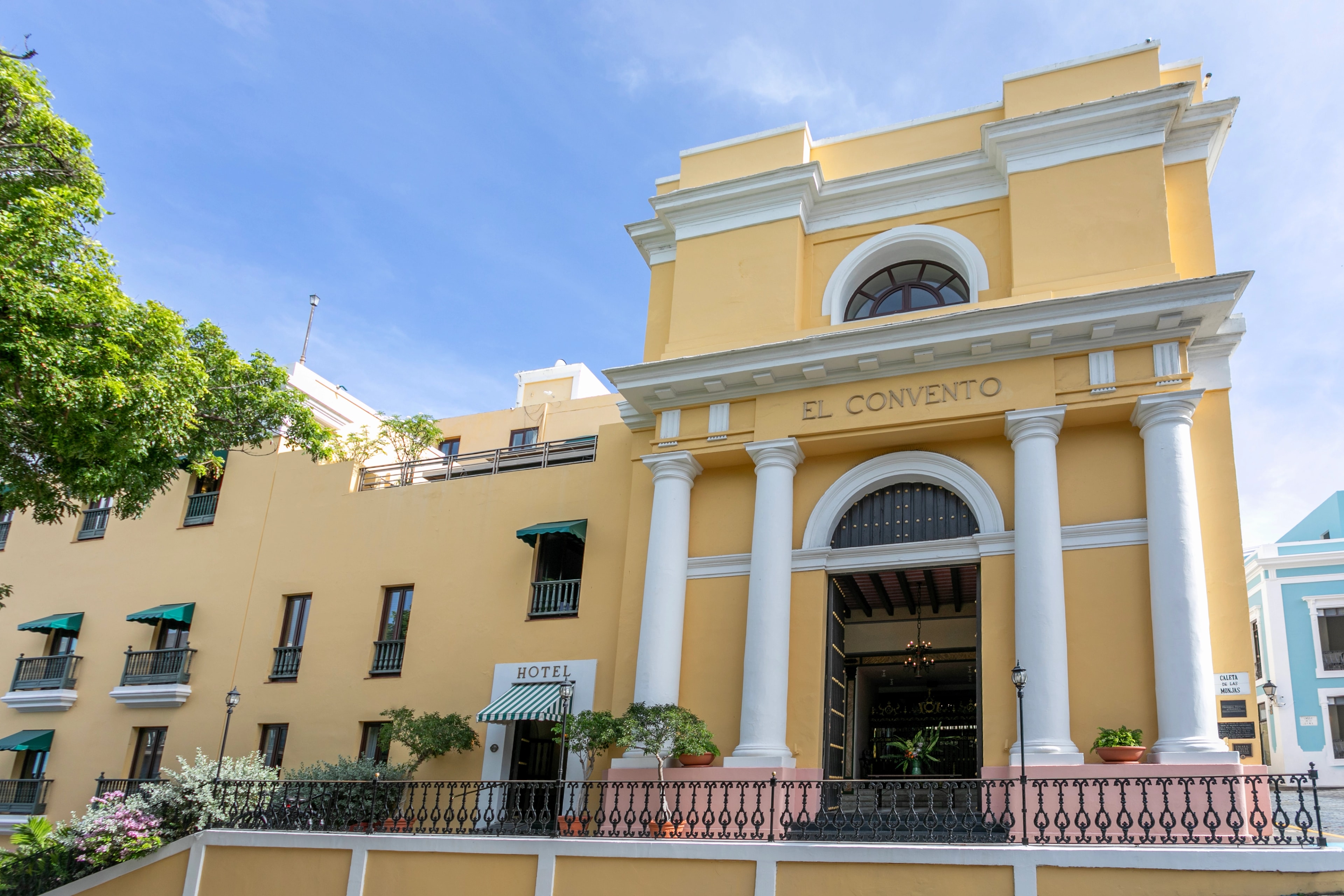 Fachada del Hotel El Convento en el Viejo San Juan, con su arquitectura colonial española en color amarillo, columnas blancas, balcones con toldos verdes y la entrada principal con el letrero "El Convento" sobre un arco.