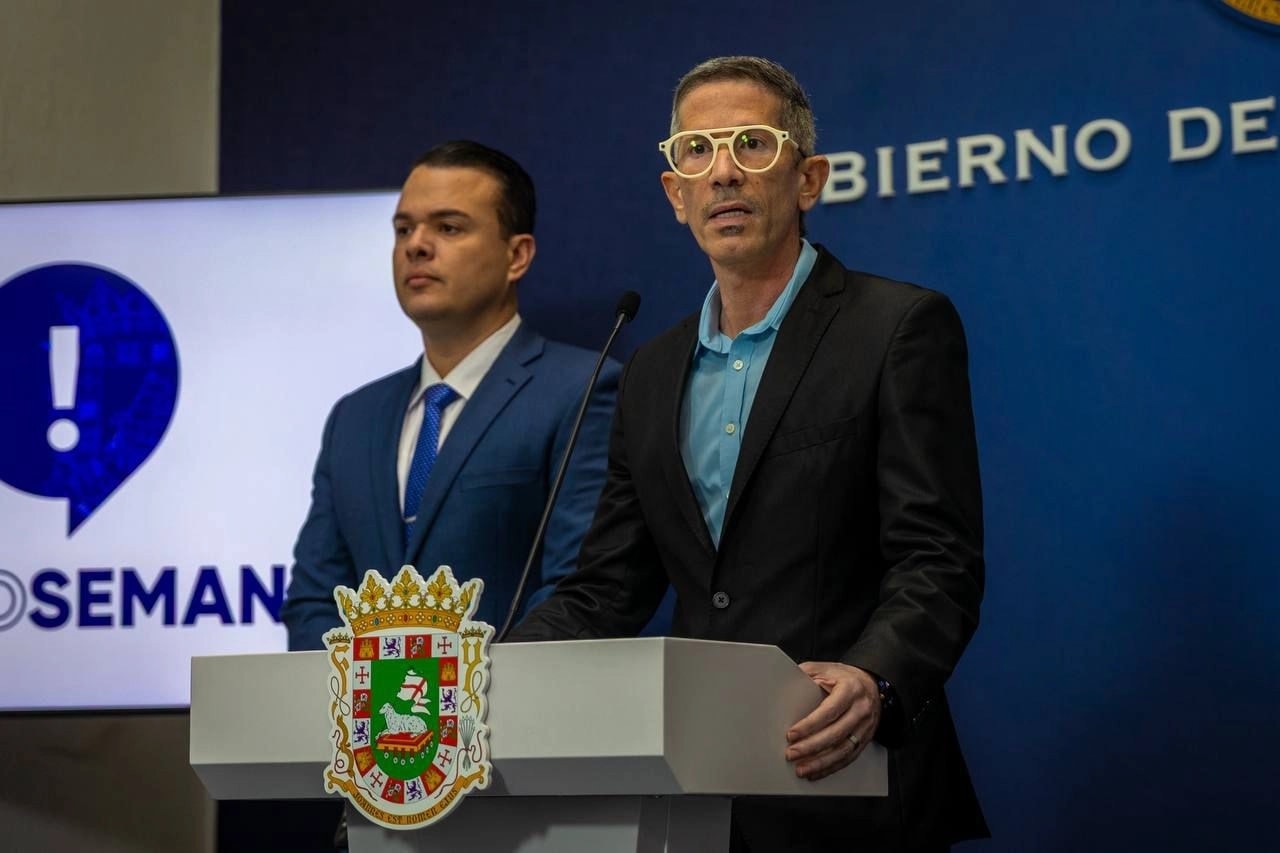 Arnaldo J. Ortiz Miranda, director ejecutivo de la Junta de Retiro del Gobierno de Puerto Rico, habla en conferencia de prensa desde un podio oficial, acompañado por otro funcionario, con el emblema del Gobierno de Puerto Rico al frente.