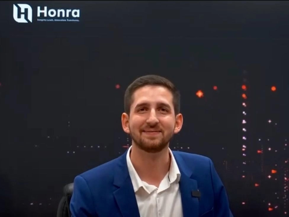 Marc A. Maceira, presidente de Honra, aparece sentado frente a un fondo oscuro con el logotipo de la empresa, vistiendo chaqueta azul y camisa clara, en una imagen corporativa.